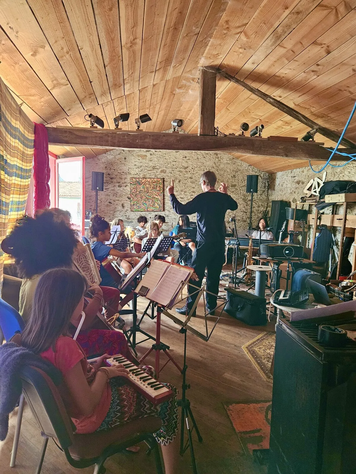 Une dizaine de jeunes musicien·nes et un chef d’orchestre, sous une charpente